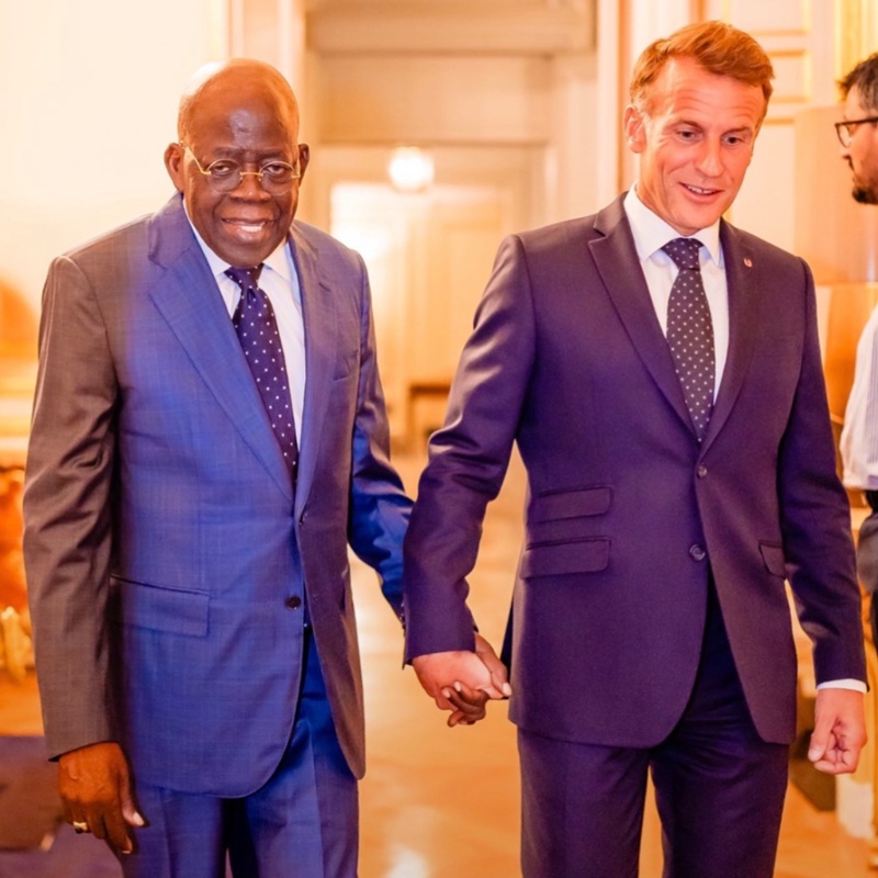 French President Emmanuel Macron holding and guiding President Bola Ahmed Tinubu by the hand